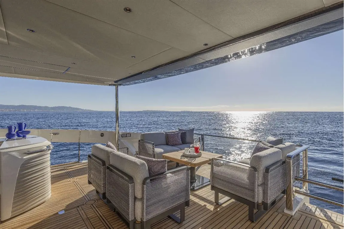 Luxurious yacht deck with plush seating, a wooden table, and ocean views under a clear sky, perfect for relaxing.